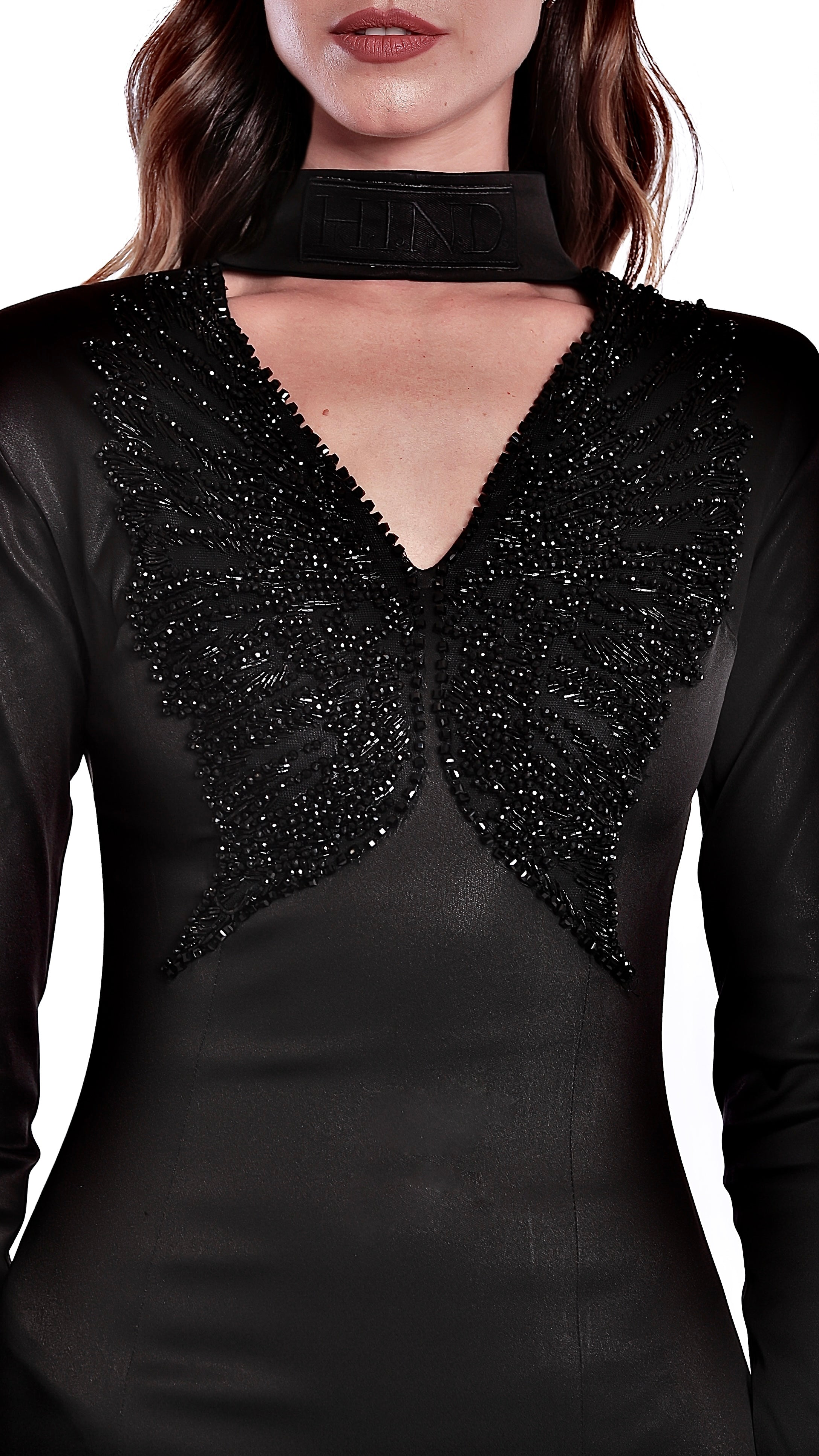 La robe Alectrona noire épouse délicatement les courbes de l’entièreté de la silhouette, agrémentée d’une broderie perlée à la main avec un fil ton sur ton.

Encolure en V accompagné de son col officier signée au nom de la maison, brodé ton sur ton.
Broderies de perles et sequins, sculptant un papillon sur la poitrine.
Épaules structurées avec rembourrage.
Manches longues tailleurs.
Une traîne lui allongeant la silhouette.
Fermeture zippée invisible au dos de 32 cm.
Coupe ajustée affinant la taille.
Soie na