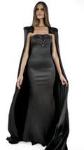 La robe longue Lampétie avec sa cape Circé en noir&nbsp;sont brodées à la main.

Robe :&nbsp;

Bustier col-cœur couvrant l’intégralité de la poitrine en la rehaussant et en épousant ses formes.
Sans bretelles ni armatures.
Arabesques de perles et sequins dessinant le cœur de la poitrine.
Fermeture zippée invisible au dos de 32 cm.
Fente au milieu du bas du dos de la robe qui couvre les chaussures.
Coupe ajustée affinant la taille.Soie naturelle d’un fini mat opaque.
Confectionnée en taille standard ou en su